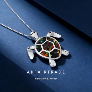 Op de afbeelding: Zilveren ketting met een schildpadhanger. De schildpad heeft een schild van mozaïek edelstenen. De ketting wordt getoond tegen een donkerblauwe achtergrond. De tekst "AKFAIRTRADE Handcrafted Jeweller" is zichtbaar.