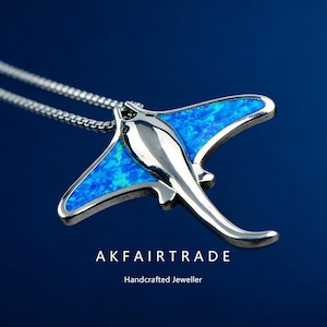 May include: A silver stingray pendant with a blue opal inlay, on a fine chain. The pendant has the text "AKFAIRTRADE" and "Handcrafted Jeweller" on a dark blue background.