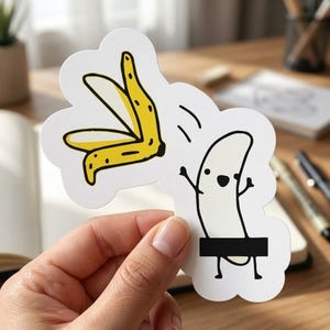 May include: A white sticker with a cartoon banana and peel design. The banana is drawn with a face and arms, and a black rectangle covers its lower half. The banana peel is yellow with black spots.