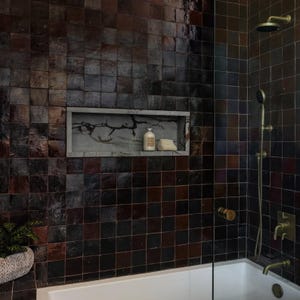 May include: A bathroom with dark brown square tiles on the walls. A recessed shelf holds a bottle and a bar of soap. A gold shower head and faucet are visible, along with a white bathtub and a small potted plant.