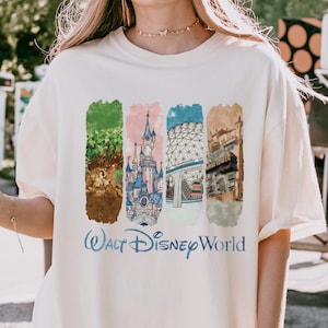 Puede incluir: Camiseta color crema con un gr&aacute;fico colorido de cuatro paneles rectangulares con im&aacute;genes de Disney World. Los paneles incluyen un castillo, un &aacute;rbol y otros elementos arquitect&oacute;nicos. Las palabras "Walt Disney World" est&aacute;n impresas en azul debajo.