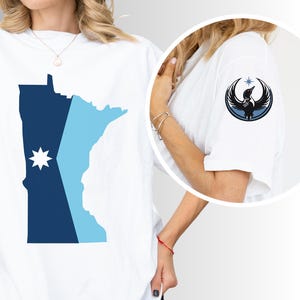 May include: White t-shirt featuring a blue and light blue graphic of a state outline with a star design. A smaller image shows a black and blue phoenix design on the sleeve. The brand name "AYATA" is printed at the bottom.