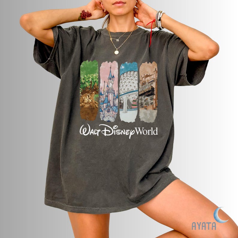 Puede incluir: Camiseta gris oscuro con cuatro im&aacute;genes rectangulares verticales que representan escenas de Disney World y las palabras "Walt Disney World" en blanco. La camiseta es de corte holgado.