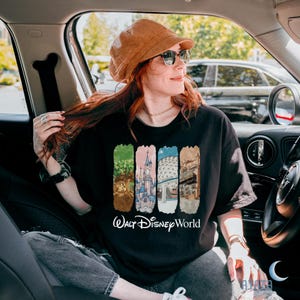 Puede incluir: Camiseta negra con un colorido gr&aacute;fico de Walt Disney World. El dise&ntilde;o presenta cuatro paneles verticales con im&aacute;genes ic&oacute;nicas del parque y las palabras "Walt Disney World" en escritura blanca. La persona de la imagen lleva un sombrero marr&oacute;n y gafas de sol.