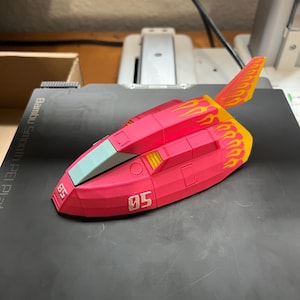 May include: A pink toy spaceship with yellow and orange flame details on the tail fin. The number "05" is printed on the side. The spaceship has a light blue windshield.