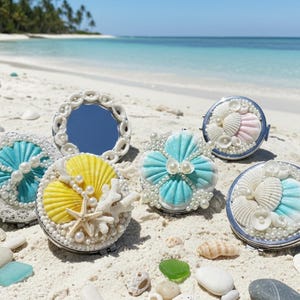 Op de afbeelding: Een assortiment decoratieve compacte spiegels en een spiegel, versierd met schelpen, parels en kant, gerangschikt op een zandstrand. De spiegels hebben verschillende kleuren, waaronder geel, blauw en wit, met de oceaan en de lucht op de achtergrond.