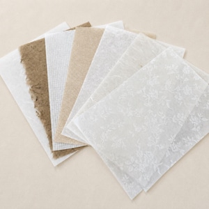 May include: A collection of rectangular paper sheets in various textures and shades, including plain white, textured brown, grid-patterned white, and translucent white paper featuring a delicate, repeating floral pattern across the surface.