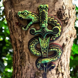 May include: A layered wooden art piece depicting a green and yellow snake coiled around a green sword. The snake's head is open, revealing its fangs. The artwork is mounted on a tree trunk, showcasing a detailed, three-dimensional design.