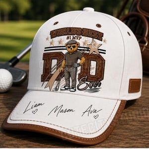 May include: A white baseball cap with a brown brim and a graphic of a teddy bear wearing sunglasses and a golf outfit. The text reads WORLD'S BEST #1 MVP DAD EVER. The brim features the handwritten names Liam, Mason, and Ava with small hearts.