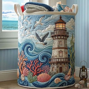 Könnte beinhalten: Ein runder Wäschekorb mit Küstenmotiv. Der Korb zeigt einen Leuchtturm, Möwen, Korallen und Meereswellen in Blau-, Korallen- und Beigetönen. Er hat weiße Griffe und ist mit gefalteten Decken gefüllt.