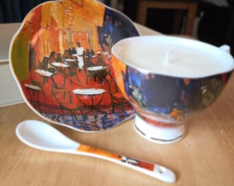 Terraza de café por la noche. Taza de porcelana, platillo y cuchara a juego con diseño clásico de Van Gogh. Vela aromática.