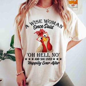 Könnte beinhalten: Cremefarbenes T-Shirt mit einem Cartoon-Huhn, das eine Brille und ein rotes Bandana trägt. Der Text "A WISE WOMAN Once Said 'OH HELL NO' AND SHE LIVED Happily Ever After" ist in schwarzer Schrift aufgedruckt.