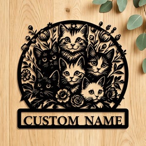 May include: Black laser-cut metal sign featuring six cat faces surrounded by floral elements. The sign includes the text "CUSTOM NAME" in a rectangular banner at the bottom. The cats have various markings and expressions.