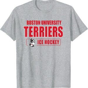 Op de afbeelding: Een grijs gemêleerd T-shirt met korte mouwen en de rode tekst BOSTON UNIVERSITY TERRIERS en ICE HOCKEY. Een afbeelding van een terriër-mascotte staat links van de tekst ICE HOCKEY, die is omkaderd door een rode rechthoekige lijn.