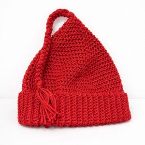 May include: A vibrant red knitted hat with a long, braided loop and tassel. The hat features a ribbed brim and a pointed top, showcasing a textured, handmade appearance. The hat is a solid color and is suitable for cold weather.
