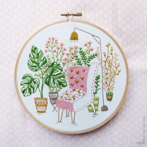 Puede incluir: Arte de bordado en aro que presenta un sill&oacute;n rosa con un patr&oacute;n floral, rodeado de plantas en macetas y una l&aacute;mpara colgante.
