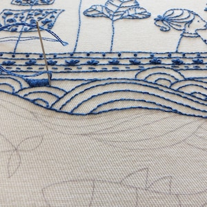 May include: Close-up of a blue embroidery design on white fabric. The design features a boat with a sail, waves, and a person standing on the boat. The embroidery is done in a simple, minimalist style.