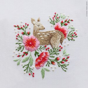 May include: Embroidered design of a brown deer with white spots surrounded by pink and red flowers with green leaves on a white background.