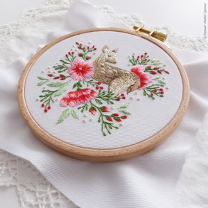 May include: Embroidered hoop art featuring a brown deer with pink and red flowers and green leaves on a white background.
