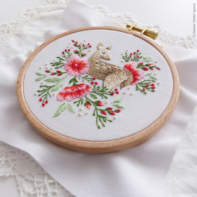 May include: Embroidered hoop art featuring a brown deer with pink and red flowers and green leaves on a white background.