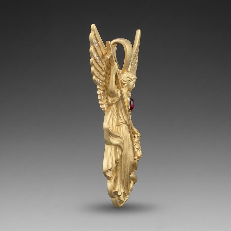 May include: A gold-colored angel pendant with outstretched wings, holding a cross. The pendant features a red gemstone and small, sparkling accents on the wings. The angel is depicted in flowing robes.