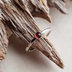 May include: A silver ring with a small, round, red gemstone set in the center.