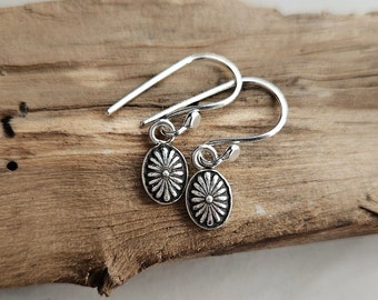 May include: A pair of silver dangle earrings with a floral design. The earrings are on a wooden surface.