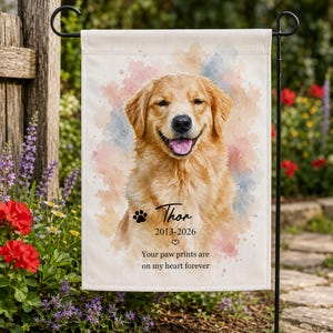May include: A rectangular garden flag featuring a watercolor-style portrait of a golden retriever with its tongue out. The text reads Thor, 2013-2026, and Your paw prints are on my heart forever, accompanied by a paw print and a small heart icon.