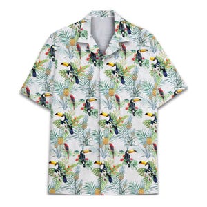 Può includere: Camicia bianca a maniche corte con motivo tropicale. Il design presenta tucani, ananas e pappagalli rossi tra il fogliame verde. La camicia ha un colletto classico e una vestibilità rilassata.