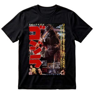 May include: A black short-sleeved t-shirt featuring a graphic print of a vintage Godzilla film poster. The design includes a large red Japanese text logo, a central image of the monster, and smaller portraits of people at the bottom with text.