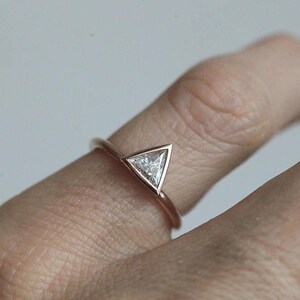 Peut inclure: Bague en or rose orn&eacute;e d'un diamant triangulaire. La bague a un fin anneau et le diamant est serti dans une monture &agrave; lunette. La bague est pr&eacute;sent&eacute;e sur un doigt, sur un fond neutre.