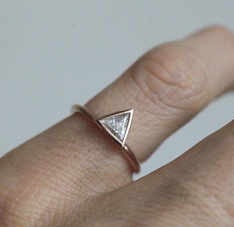Peut inclure: Bague en or rose orn&eacute;e d'un diamant triangulaire. La bague a un fin anneau et le diamant est serti dans une monture &agrave; lunette. La bague est pr&eacute;sent&eacute;e sur un doigt, sur un fond neutre.