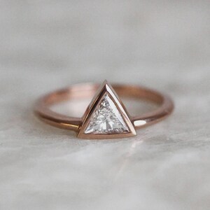 Peut inclure: Bague en or rose avec un diamant taill&eacute; en triangle. Le diamant est serti dans un sertissage &agrave; lunette, et le bracelet est en or rose fin et poli. La bague est pr&eacute;sent&eacute;e sur une surface de couleur claire.