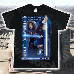 Può includere: T-shirt nera con un design grafico blu raffigurante una donna con una spada laser blu. Il design include il testo "SKYWALKER" e altro testo in un font futuristico. L'immagine ha un tema fantascientifico.