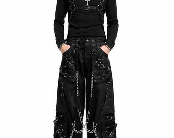 May include: Black outfit featuring a long-sleeved shirt, wide-leg pants, and accessories. The shirt has a harness-style design. The pants have multiple pockets, chains, and metal accents. The outfit is all black, creating a gothic or alternative aesthetic.