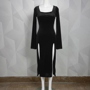 Op de afbeelding: Een zwarte jurk met lange mouwen, een vierkante halslijn en twee hoge splitten aan de voorkant. De jurk wordt op een mannequin gepresenteerd. De jurk is gemaakt van een zacht, fluweelachtig materiaal.