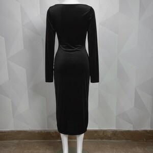 Op de afbeelding: Een lange zwarte jurk met lange mouwen en een zoom tot op de knie. De jurk heeft een ronde hals en een getailleerd silhouet. De jurk wordt gepresenteerd op een mannequin tegen een witte geometrisch patroon muur.
