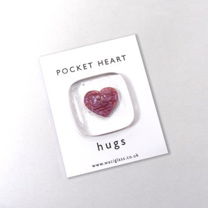 May include: A small glass square with a pink heart inside. The square has the words "Pocket Heart" and "hugs" on it. The text below the heart reads "www.waciglass.co.uk".