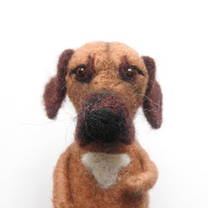 May include: A brown and black felt dog toy with brown eyes and a white patch on its chest.
