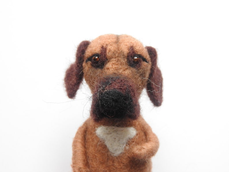 May include: A brown and black felt dog toy with brown eyes and a white patch on its chest.