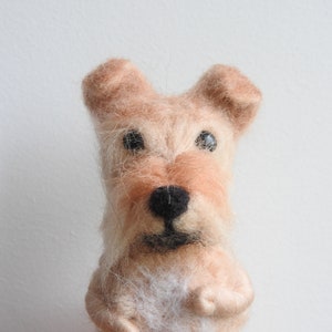 May include: A hand-felted dog figurine with a light brown and cream colored coat. The dog has black eyes and a black nose.