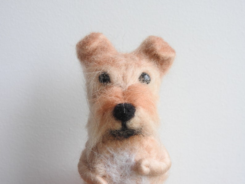 May include: A hand-felted dog figurine with a light brown and cream colored coat. The dog has black eyes and a black nose.