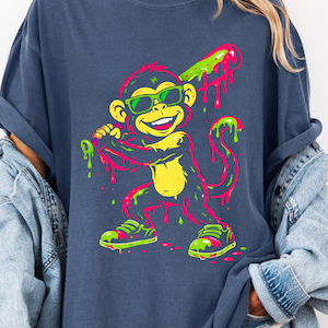 May include: Navy blue t-shirt featuring a cartoon monkey wearing sunglasses and holding a baseball bat. The monkey is depicted in neon green, pink, and yellow colors. The shirt has a relaxed fit.