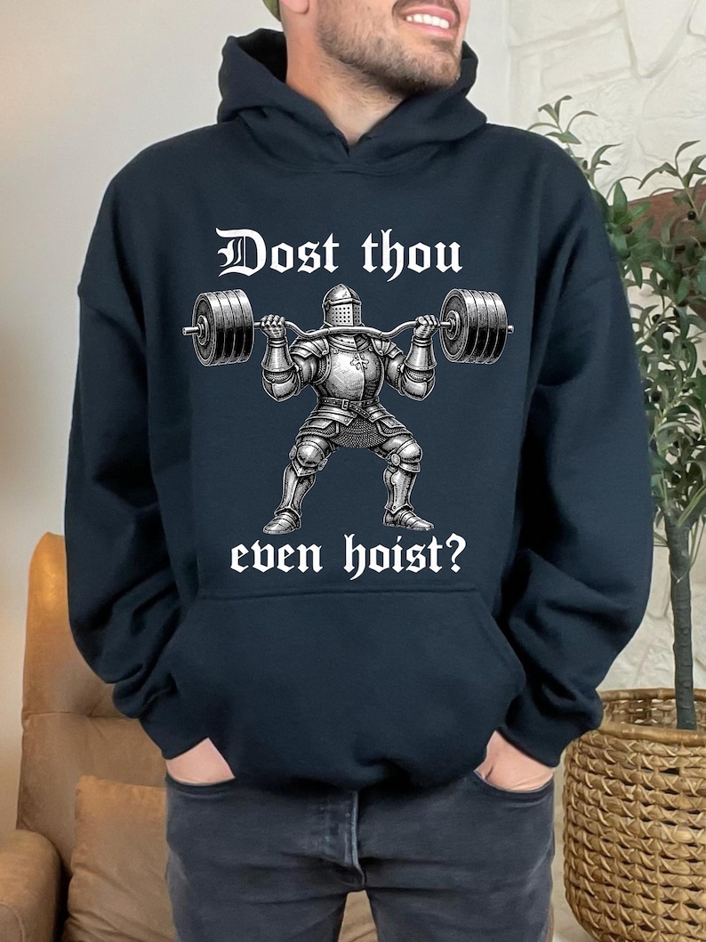 K&ouml;nnte beinhalten: Schwarzer Kapuzenpullover mit einem Gewichtheber-Ritter-Motiv. Der Ritter, in R&uuml;stung, hebt eine Langhantel. Der Text "Dost thou even hoist?" ist in wei&szlig;er gotischer Schrift &uuml;ber und unter dem Ritter gedruckt.
