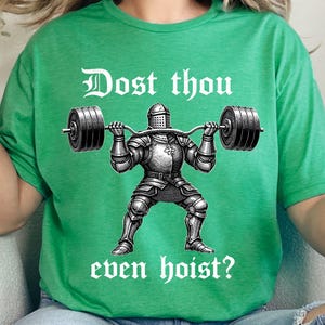K&ouml;nnte beinhalten: Gr&uuml;nes T-Shirt mit einer Schwarz-Wei&szlig;-Illustration eines Ritters, der eine Langhantel hebt. Der Text "Dost thou even hoist?" ist oberhalb und unterhalb des Ritterbildes in einer mittelalterlichen Schrift gedruckt.
