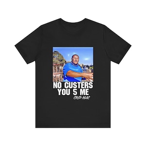 May include: Black t-shirt featuring a graphic of a man in a blue shirt with the text "NO CUSTERS YOU 5 ME" and "CRIP MAC" in white. The image is set against a blue sky background.
