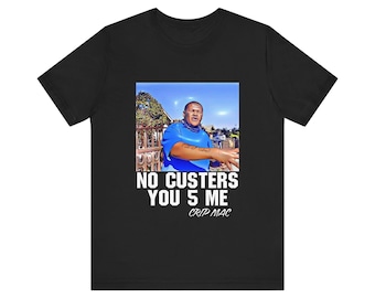 May include: Black t-shirt featuring a graphic of a man in a blue shirt with the text "NO CUSTERS YOU 5 ME" and "CRIP MAC" in white. The image is set against a blue sky background.