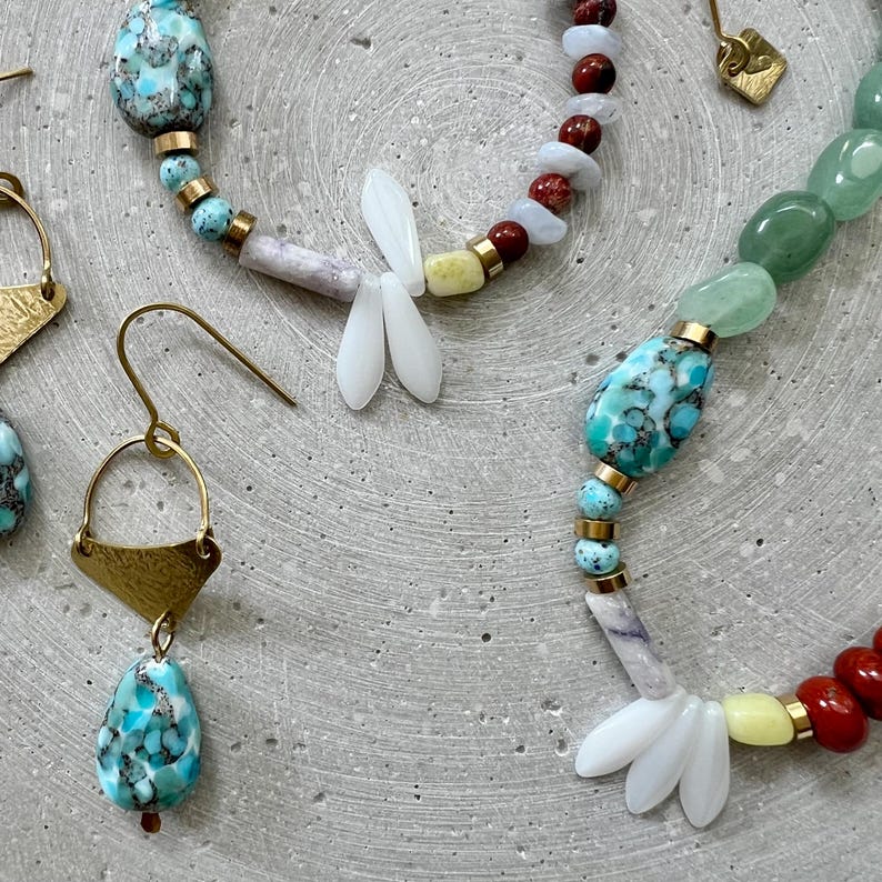 May include: Close-up of artisan jewellery featuring turquoise, green, red, and white beads. The jewellery includes earrings with gold-coloured metal accents and a necklace with a dragonfly-shaped pendant. The beads are strung together with gold-coloured metal spacers.