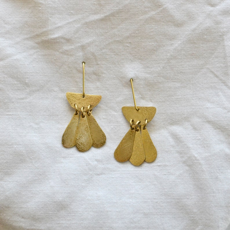 May include: A pair of gold-toned earrings with a teardrop shape and a crescent moon design. The earrings are made of metal and have a hammered texture.