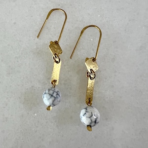 K&ouml;nnte beinhalten: Goldene Ohrh&auml;nger mit wei&szlig;en marmorartigen Perlen und goldenen geometrischen Formen.